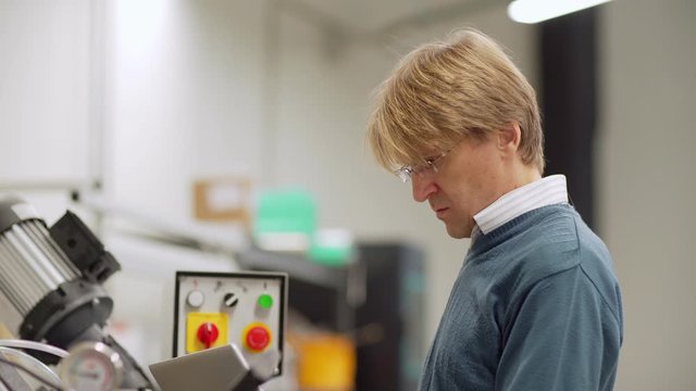 Tilt up side view shot of middle aged engineer in eyeglasses using laptop computer standing by cnc machine in factory laboratory