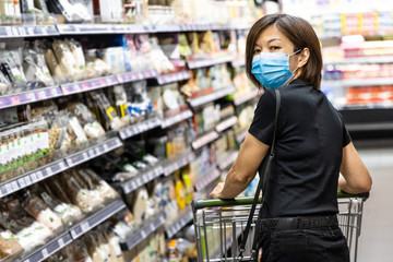Asian woman shopping groceries in supermarket with protective face mask as new normal requirement