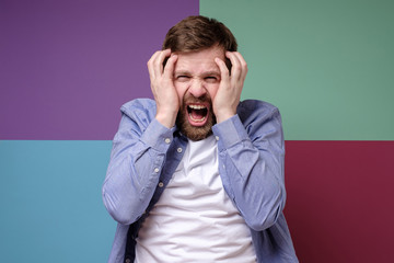 Caucasian bearded man in stress, he screams and grabs his head with hands.