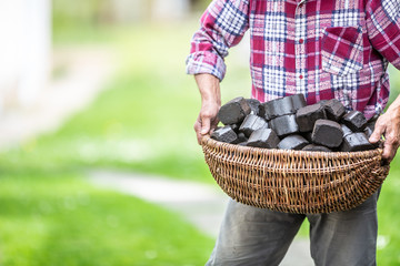 Man carrying basket full of coal briquettes in the backyard of his house