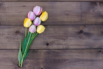 Pink and yellow tulips on a dark wooden background. Bouquet of fresh flowers. Top view
