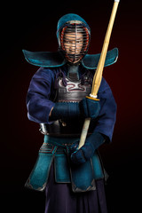 Portrait of man kendo fighter with shinai (bamboo sword). Shot in studio. Isolated with clipping path on dark red background