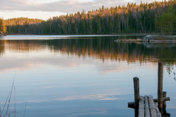 The old wooden pier on a lake in spring forest. Trees and sky reflected in the calm waters of a forest lake. Natural background. Sunset moment. island in the lake. Stump. Evening forest 