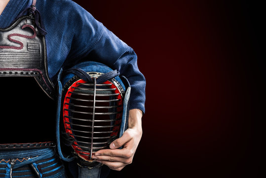 male in in tradition kendo armor with helmet in hand. shot in studio. isolated on dark red background
