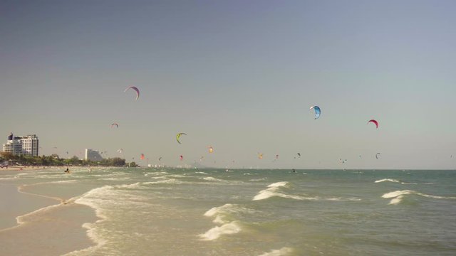 the camera goes into the sea on a sandy beach and shows a lot of kiters on a summer day. small waves on the sea against the background of modern hotels. Thailand, main beach Hua Hin