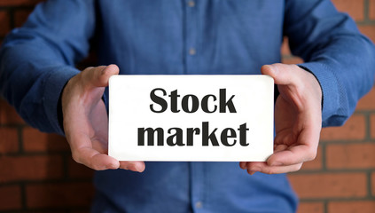 Stock market text on a white sign in two hands of a man in a blue shirt