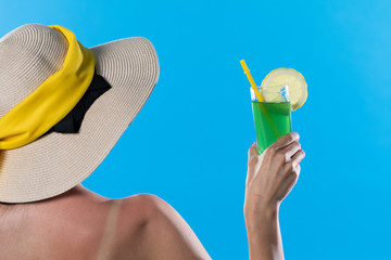 The teenager turned her back with a hat on her head and hand holds a glass with a cool drink on a sunny day.