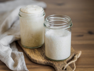 Two glass jars with wheat sourdough starters in different hydration levels. Starter 100 percent hydration in the background and starter with higher hydration in the foreground. Copy space