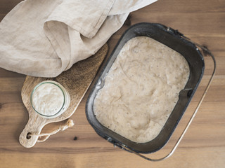 Wheat sourdough starter in glass jar and sourdough in bread pan of bread maker machine. Homemade breadmaking concept