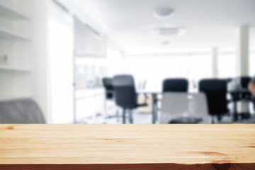 Empty wooden desk space over blurred office or meeting room background. Product display.