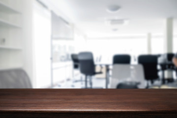 Empty wooden desk space over blurred office or meeting room background. Product display.