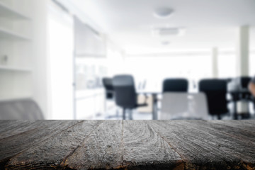Empty wooden desk space over blurred office or meeting room background. Product display.