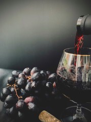 Glass of red wine and dark grapes on a black background. Wine is pouring into a glass. Macro shot.