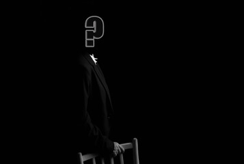 A faceless, thoughtful businessman with a question mark for a head stands half-turned, leaning on a chair. Copy of the space, banner, black isolated background.
