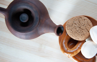Clay teapot,  a brown saucer with fresh marshmallows, cookies and bagels on a light wooden table along , tea party, chocolate shades
