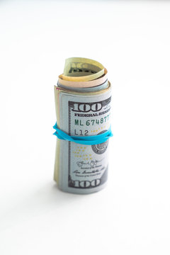 Close up photograph of a rolled up wad of cash on edge with a blue rubber band wrapped around with hundred dollar bill on top isolated on a white background with copy space.