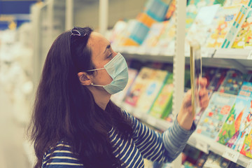 Woman in medical mask choosing goods in a store. Concept of shopping during quarantine at covid-19 pandemic. shopping at the time of the coronavirus. Beautiful young women in a flu mask. toned