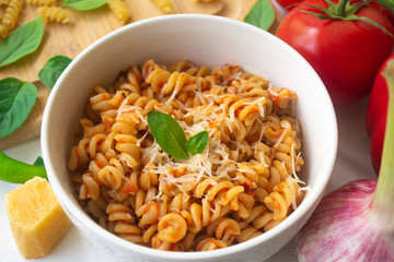 Italian pasta fusilli with fresh and spicy tomato sauce, Parmesan cheese and basil with ingredients in the background - tomatoes, garlic, paprika, dry pasta, Parmesan cheese and basil leaves