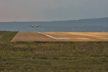 Landing airplane in the far distance litted by golden light of sunset. Transpotration concept. Copy space