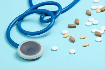 Bottle with different pills and a stethoscope on blue background. Medical cardiological still life. Top view