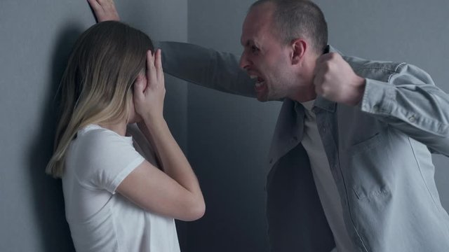 Angry husband trying to hit his wife indoors. Concept of domestic violence