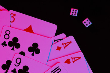 Playing cards with dice in neon blue-pink light on a black background. Game addiction. Poker