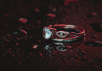 Gold rings with a diamond in blue-red neon light on a dark background with drops of water