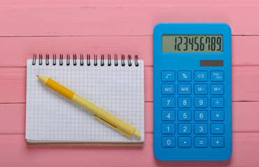 Blue calculator with notebook on pink wooden background. Top view