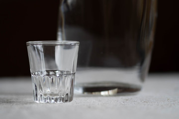 a small crystal glass with a decanter on a dark background. bottle of vodka
