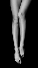black and white photo of female legs lying on a black void and pulling toes, top view isolated on black background