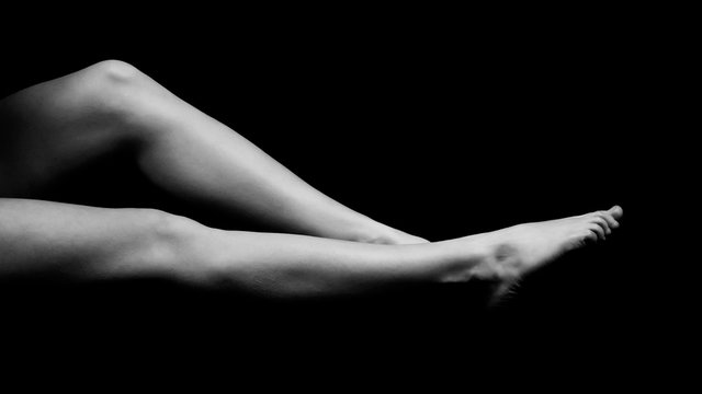black and white photo of female legs lying on a black void and pulling toes, side view isolated on black background