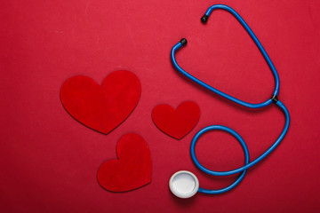 Stethoscope with hearts on red background. Top view