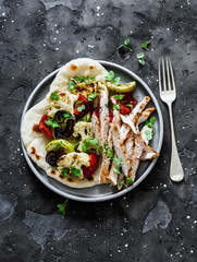 Naan flatbread with grilled vegetables and turkey on a dark background, top view