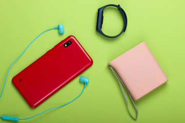 Modern gadgets. Smartphone and smart bracelet, power bank, vacuum earphones on green background. Top view