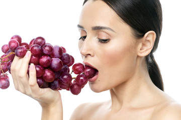 close-up portrait of a girl with clear skin and big brown eyes with soft makeup, with red grapes on a white background