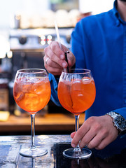 Aperol is an alcoholic cocktail. Orange. Cold drink with ice cubes. The glass is on the bar. A male bartender stirs a cocktail. Menu for restaurants, cafes and bars.