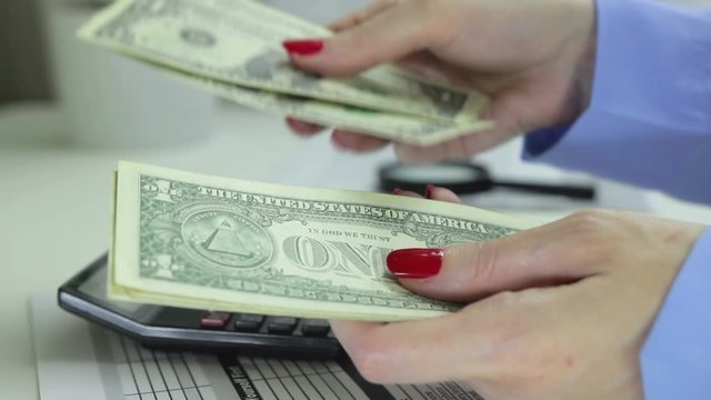 Woman counts cash on a backround of a desk with a calculator, coins, magnifier