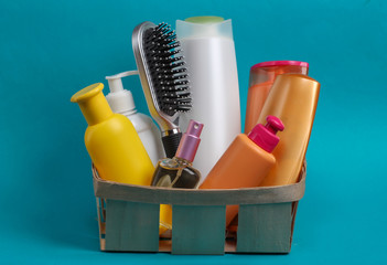 Bottles of cosmetics, shampoos, comb in a wooden basket on blue background. Beauty products