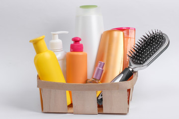 Bottles of cosmetics, shampoos, comb in a wooden basket on white background. Beauty products