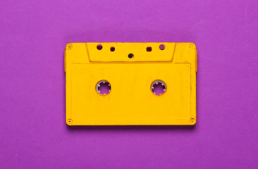 Yellow audio cassette on purple background. 80s. Top view