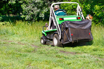Obraz premium A utility service worker looks after the lawn and mows the grass with a tractor lawn mower.