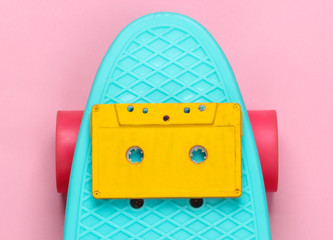 Cruiser board with audio cassette on a pink pastel background. 80s fun. Top view