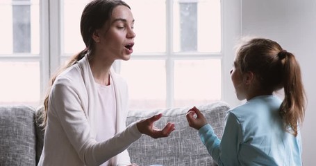 Concentrated young professional speech therapist teaching little child girl with voice problems. Mixed race mommy practicing foreign language words pronunciation with small daughter in living room.