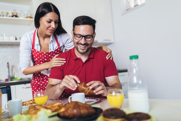 Cheerful young couple having breakfast in kitchen at home.
