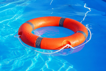 Red lifebuoy pool ring float on blue water. Life ring floating on top of sunny blue water. Life ring in swimming pool.
