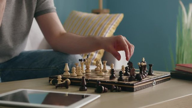 Wooden chess board with man-carved pieces is on the coffee table, man is playing chess alone, trying to entertian in self-isolation, but missing close people, Close up, Slow motion.