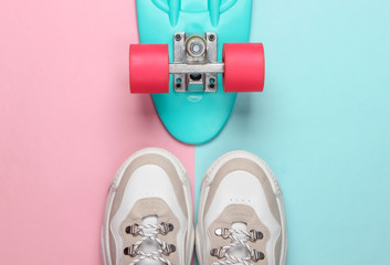 Fashionable sneakers with cruiser board on pink blue pastel background. Youth fun. Top view. Minimalism
