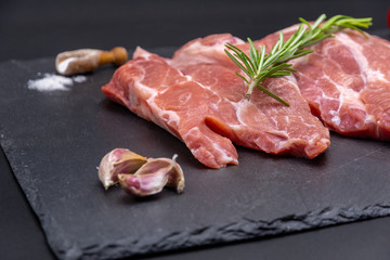 pork raw steak and ingredients on black slate