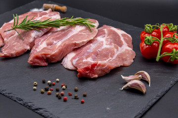 pork raw steak and ingredients on black slate