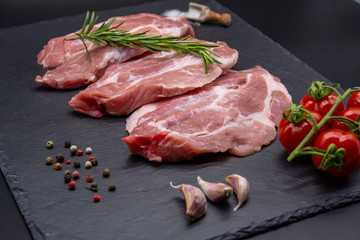 pork raw steak and ingredients on black slate